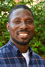 Adebayo Adeoti headshot. Student is wearing a dark blue patterned shirt in front of green foliage