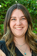 Fisher EasleySmith headshot. She is wearing a black shirt in front of green foliage.
