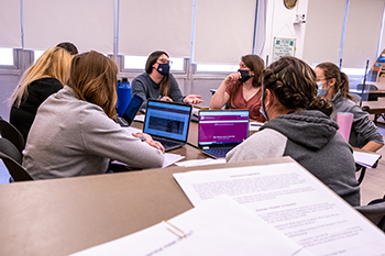 Image of a group of students chatting and collaborating while sitting around a table in a classroom